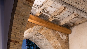 Un plafond en pierre en forme d’arc surmonté d’une poutre en bois, un mur blanc et une plante en pot.