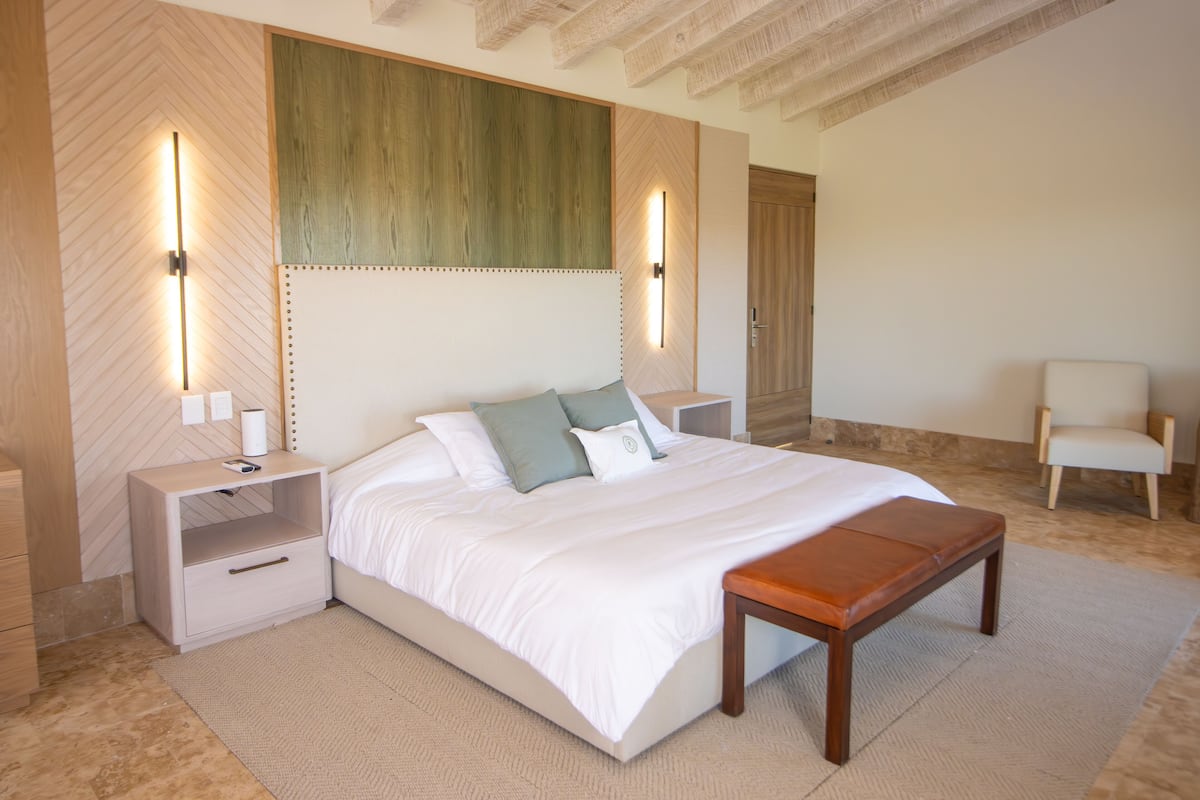 A bedroom with a large bed, bedside tables, a bench, and a chair.