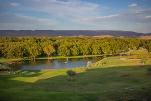 Un parcours de golf avec un étang, des arbres et des montagnes à l’horizon.