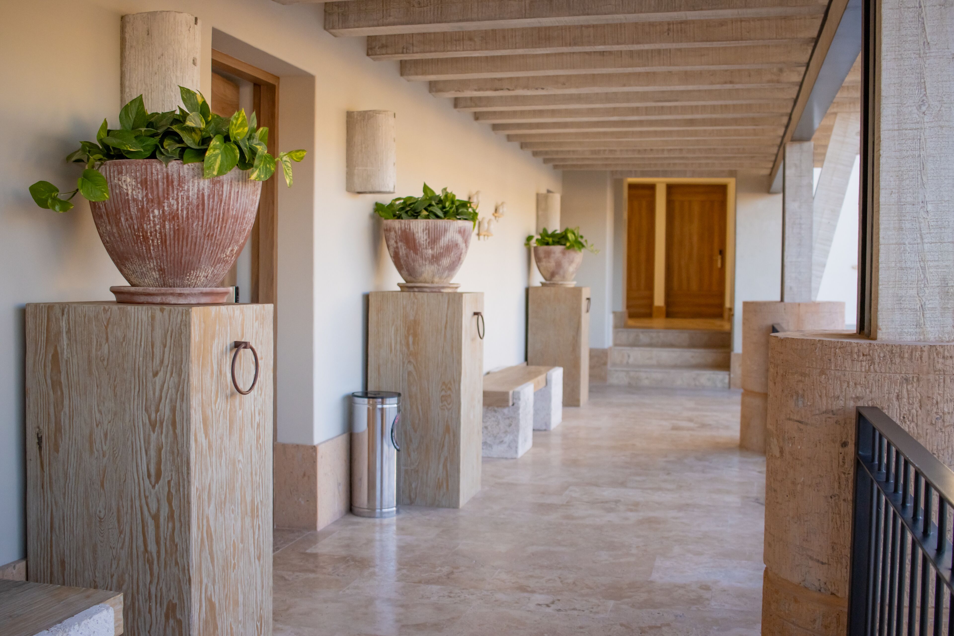 Un pasillo con grandes macetas de terracota, columnas de madera y piso de baldosas.