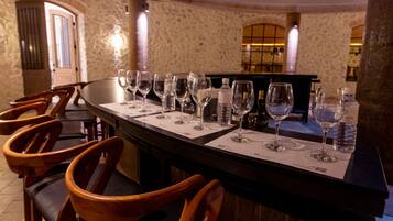 A bar area with wooden chairs and a long table set with wine glasses and water bottles.