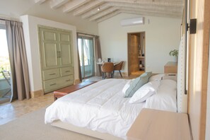 Une chambre avec un grand lit, un bureau avec une chaise, une armoire et une salle de bain visible à travers une porte ouverte.