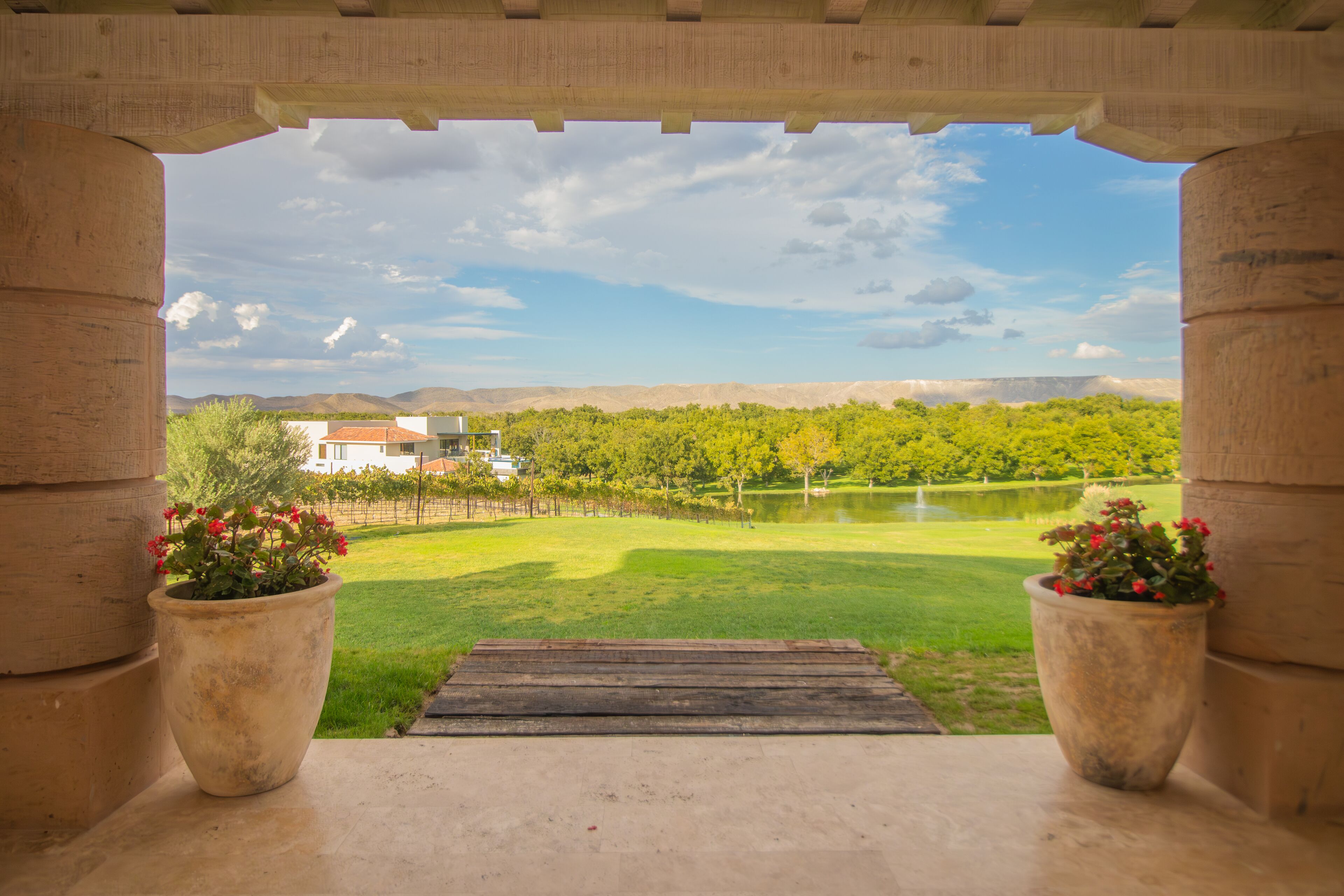 A view through an archway with a paved area leading to a grassy field and a body of water.