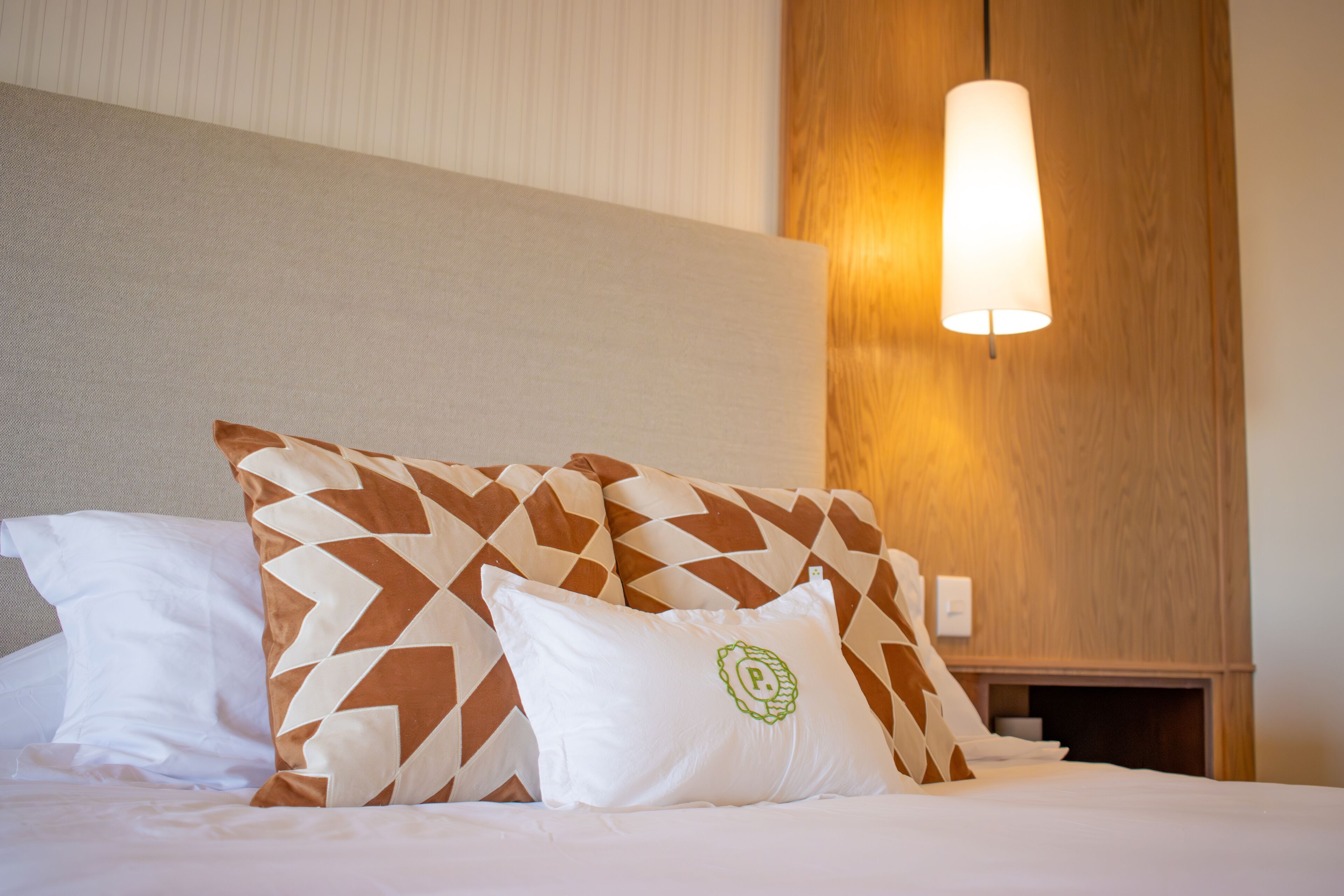 Un letto rifatto con cuscini decorati e una lampada a sospensione.