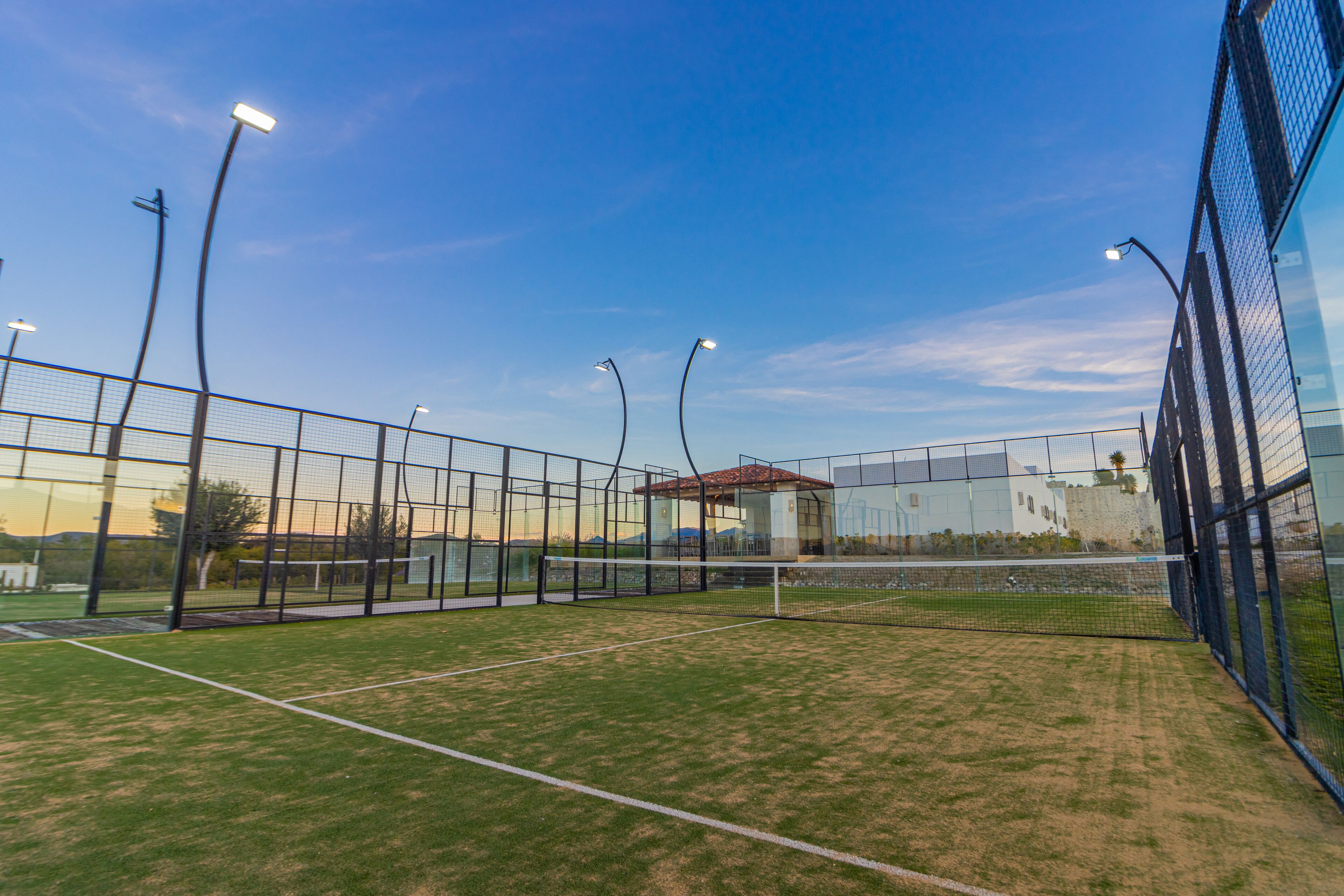 A tennis court with a net, surrounded by a fence and street lamps.