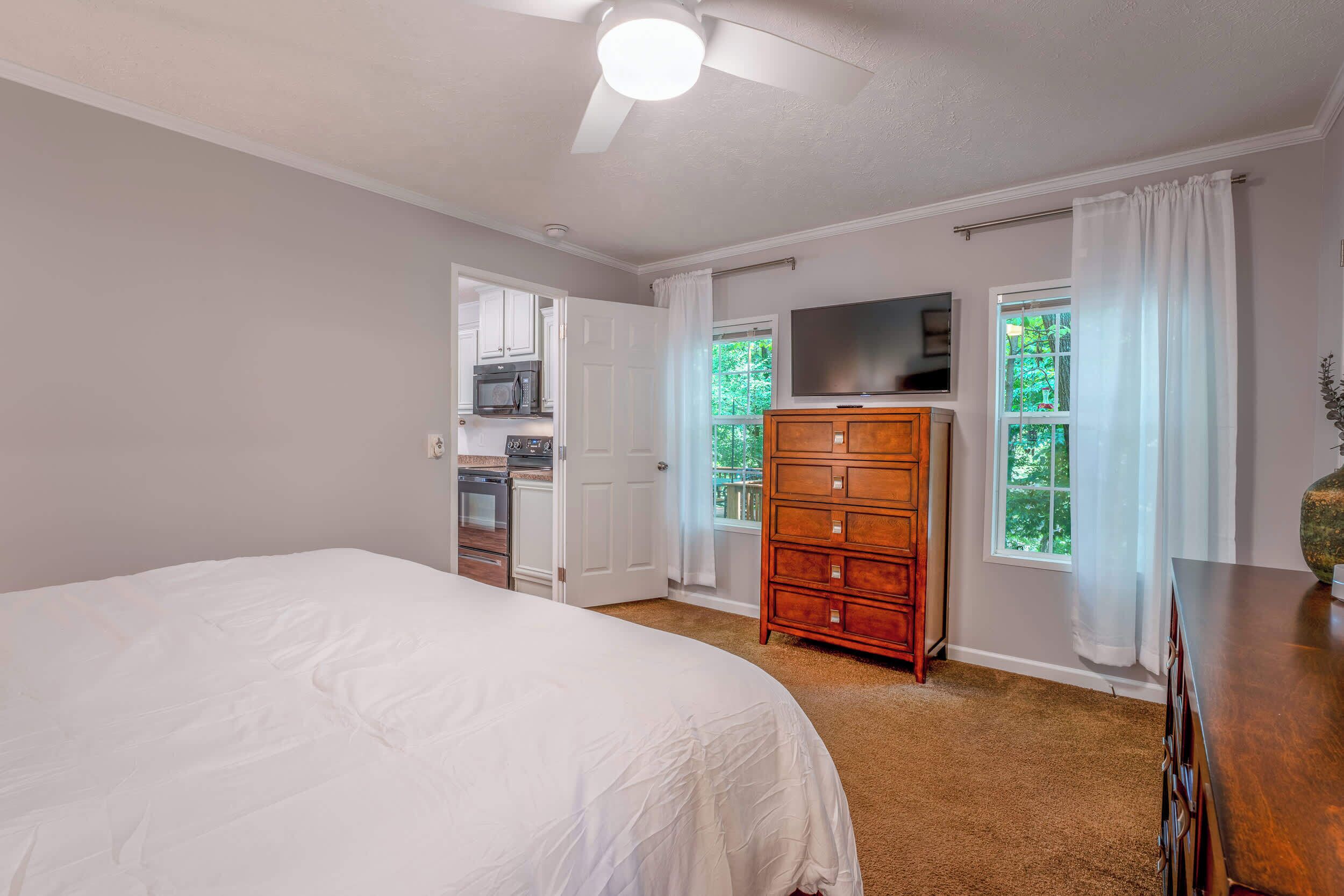 A bedroom with a large bed, a wooden dresser, a television, and a view of a balcony.