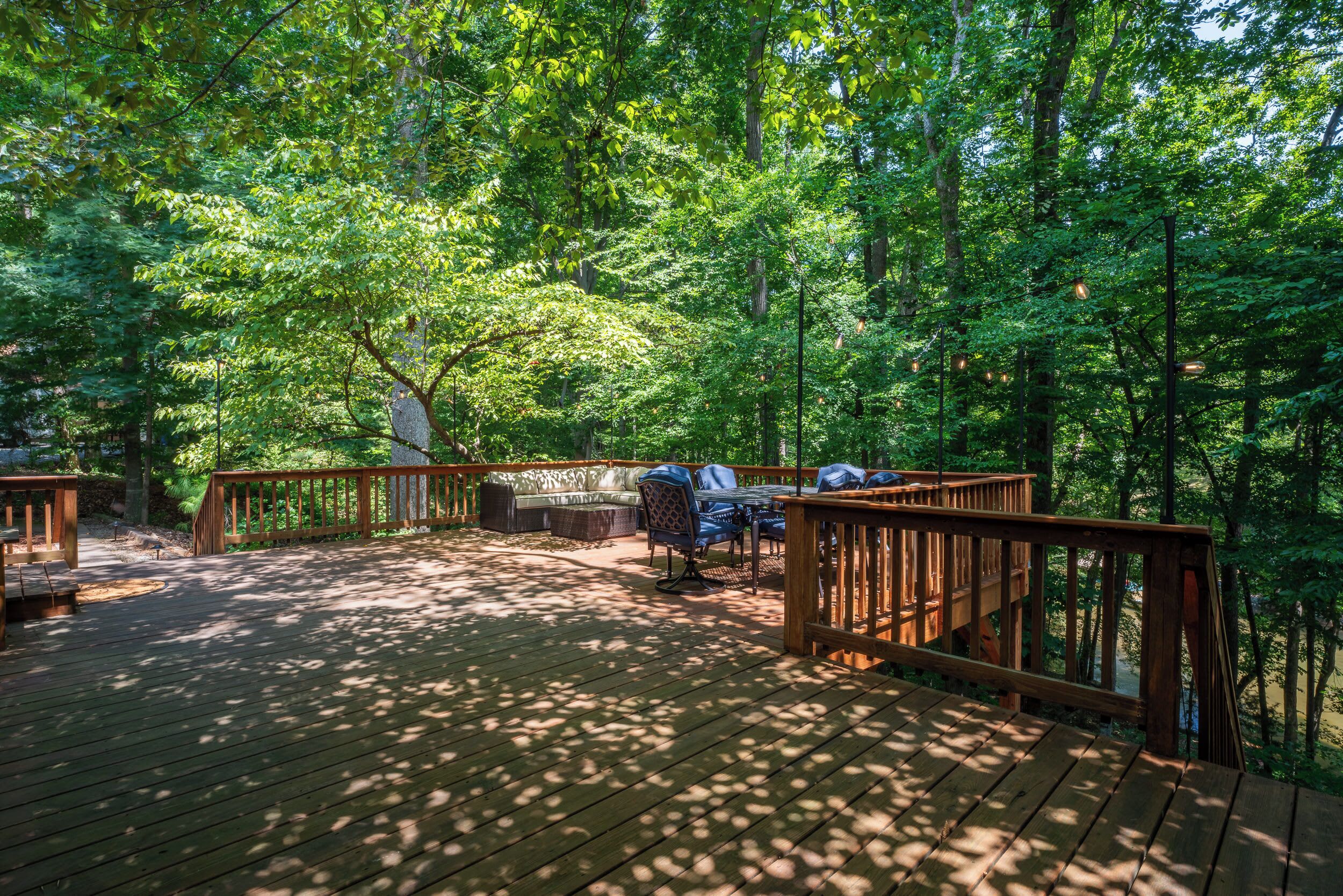 A wooden deck with outdoor furniture, surrounded by dense forest.