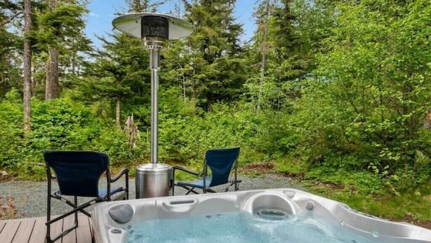 A hot tub with two chairs and a table, surrounded by a deck and dense greenery. - Cozy 2BR Apt, Hot tub, King bed, secluded, and freshly remodeled!
 (Juneau)