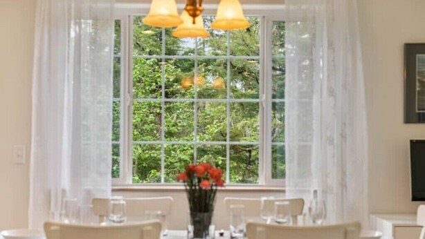 Un'area pranzo con un tavolo apparecchiato per quattro persone, un vaso di fiori e una finestra vista verde.