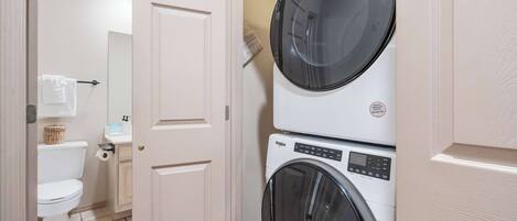 A laundry room with a stacked washer and dryer, a toilet, and a sink.