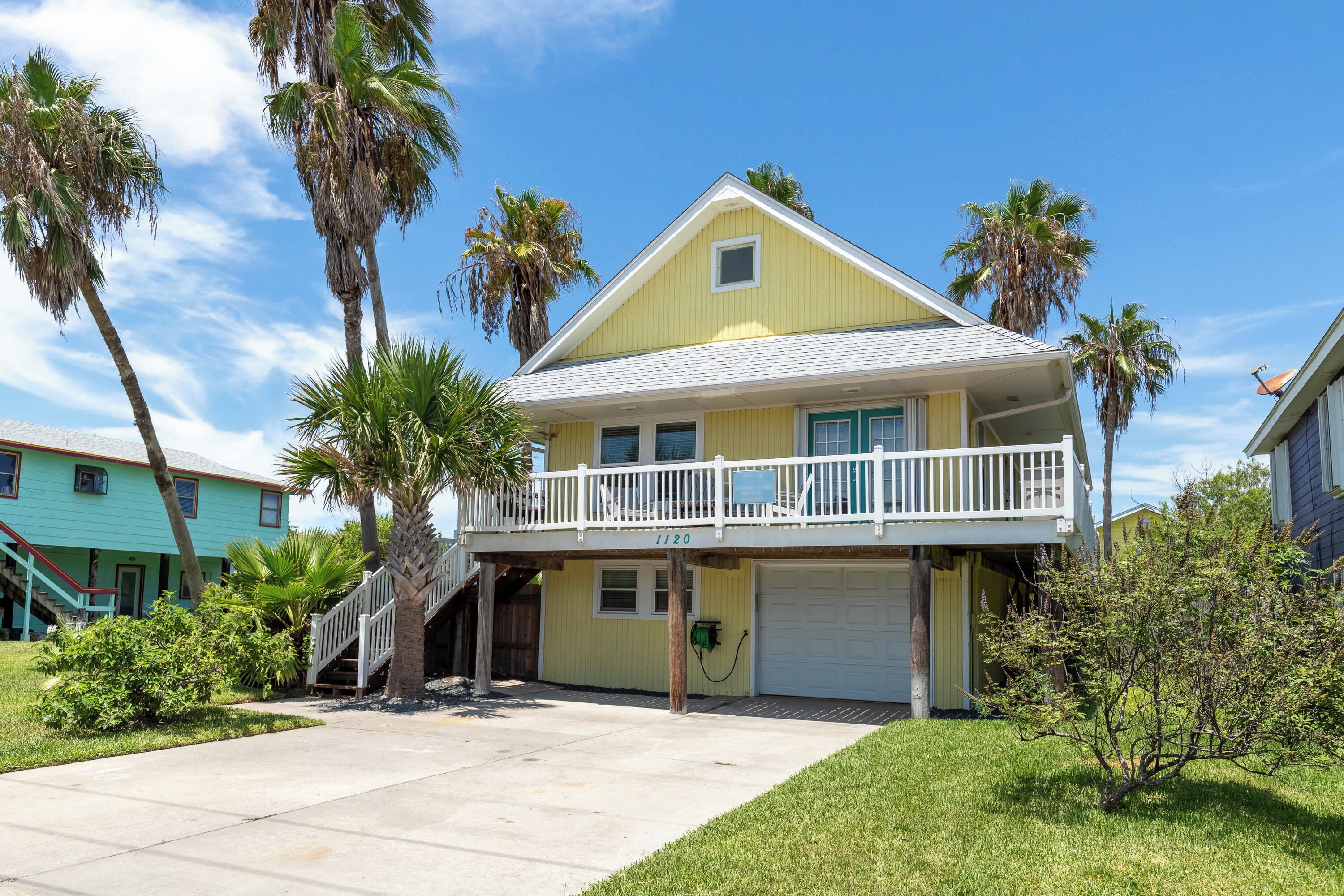 A two-story house with a balcony, a garage, and a small front yard with palm trees.
