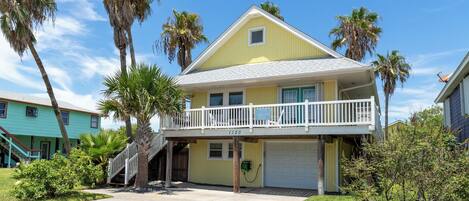 A two-story house with a balcony, a garage, and a small front yard with palm trees.