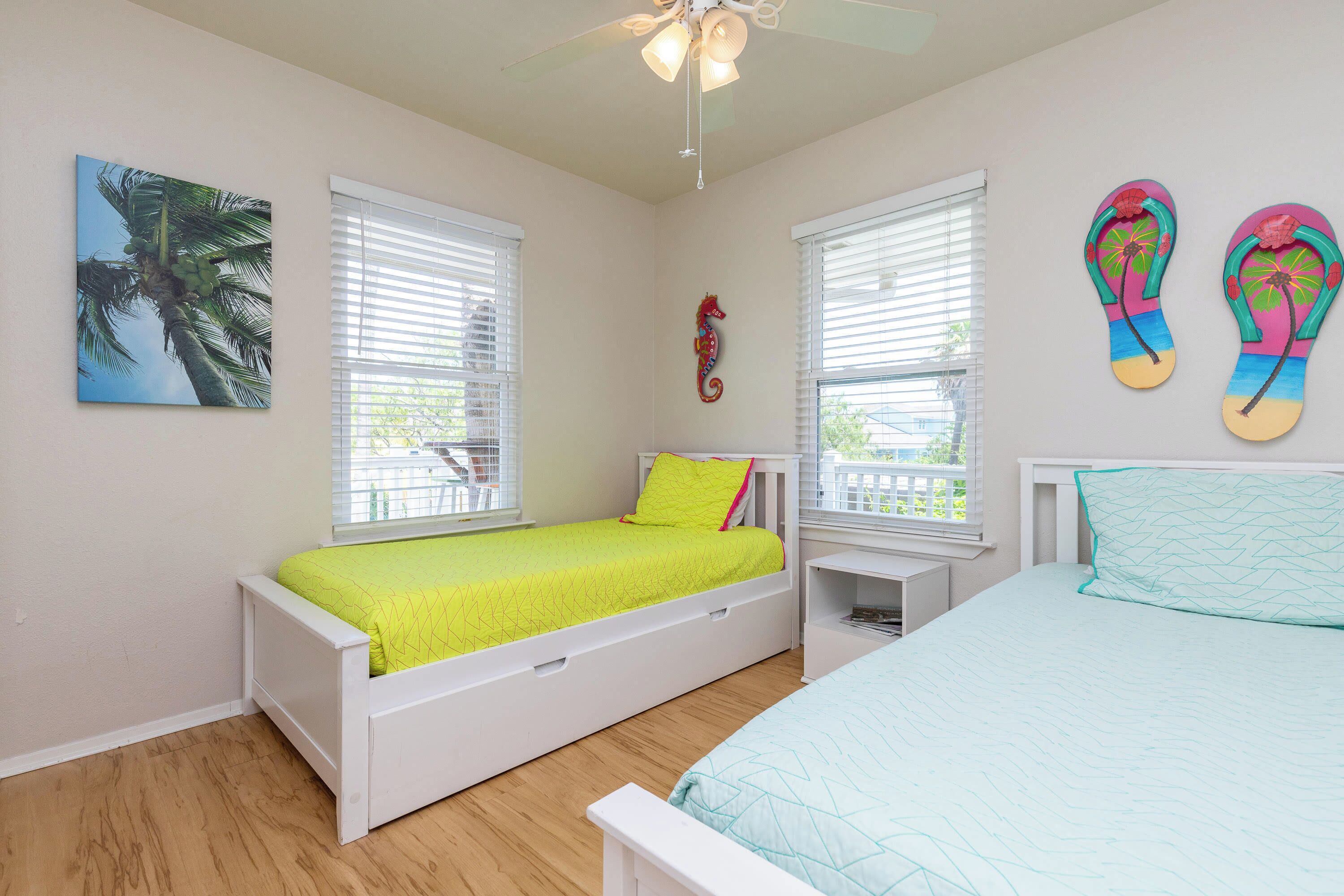 A bedroom with two beds, a ceiling fan, and a window with blinds.