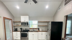 Eine moderne Küche mit weißen Schränken, einem schwarzen Kühlschrank und einem Deckenventilator.