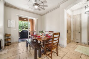 A dining area with a wooden table set for four, a ceiling fan, and a view of the outdoors through a glass door.