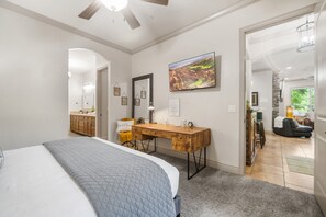 A bedroom with a bed, a wooden desk, a mirror, and a painting on the wall.