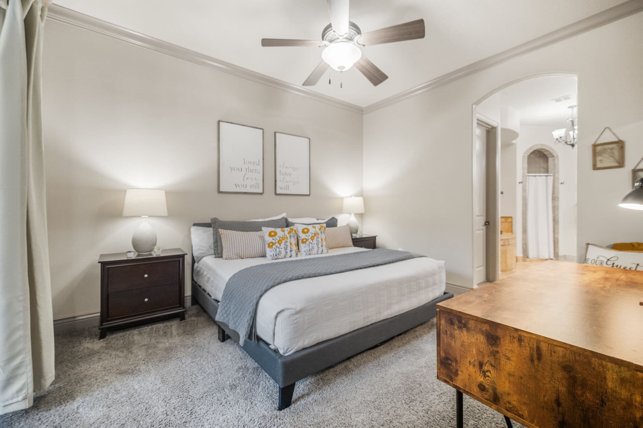 A bedroom with a bed, nightstands, a wooden dresser, a ceiling fan, and two framed quotes on the wall.