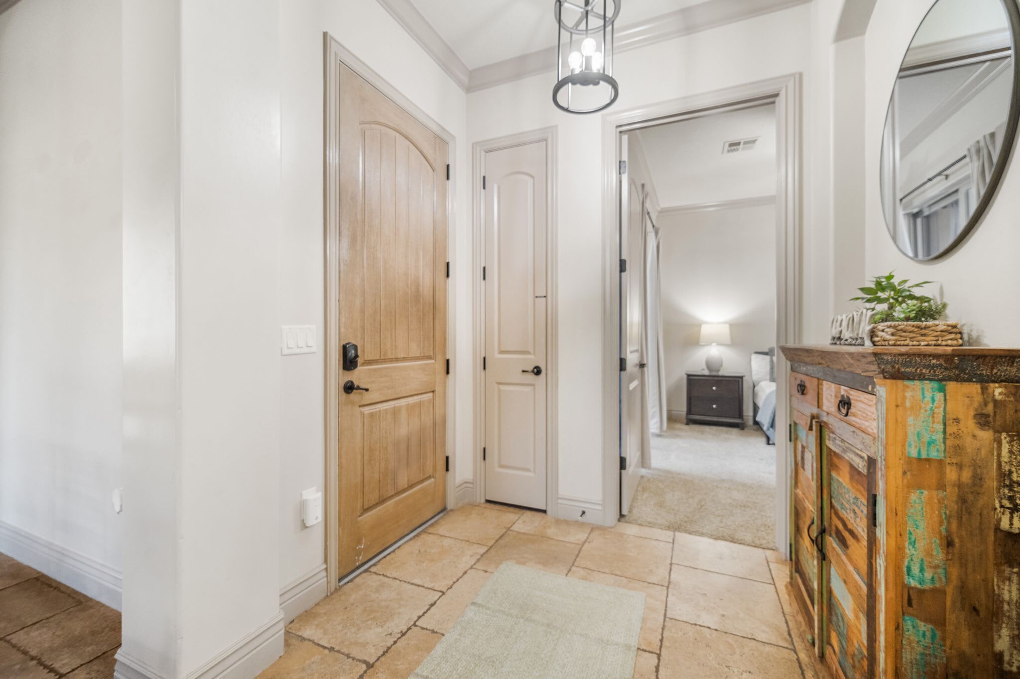 A hallway with a wooden door, a white wall, a mirror, and a cabinet with a rustic design.