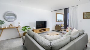 Una sala de estar moderna con un sofá gris, un mueble de televisión de madera y un espejo grande.