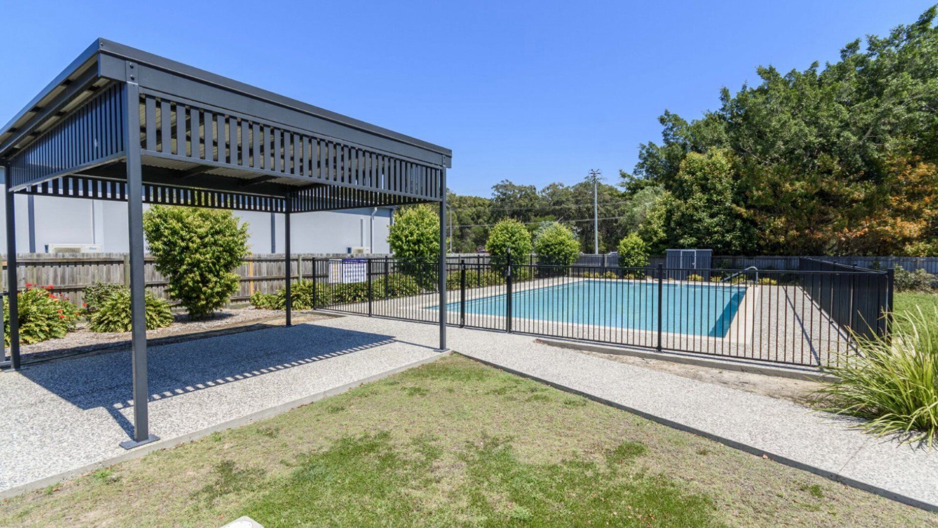 A covered outdoor area with a pool, surrounded by a fence and greenery.