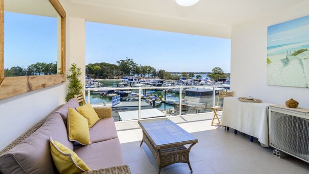 Un balcón con vista a un puerto deportivo, un sofá de mimbre, una mesa y un cuadro en la pared.