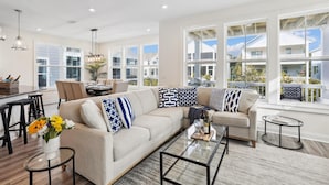A spacious living room with a large beige sectional sofa, a glass coffee table, and a dining area with a white table and chairs.