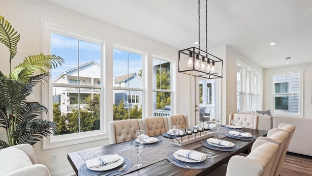 A dining area with a long table set for six, large windows, and a view of neighboring houses.