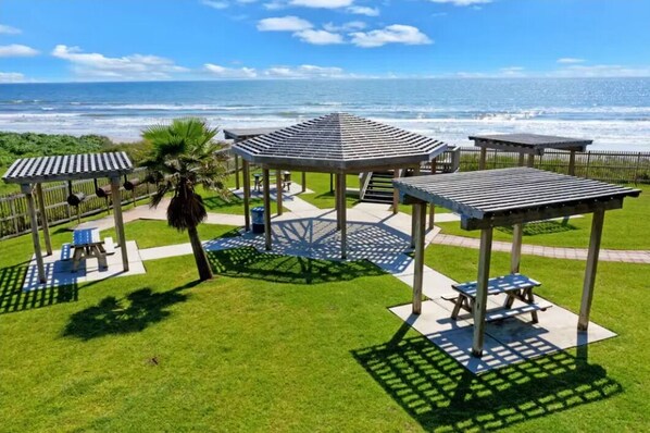 Un parque junto a la playa con gazebos, mesas de picnic y vistas al océano.
