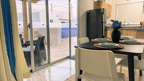 Eine moderne Küche mit einem schwarzen Kühlschrank, einem gedeckten Esstisch und einem Blumenstrauß, mit Blick auf einen blau gefliesten Pool durch Glastüren.