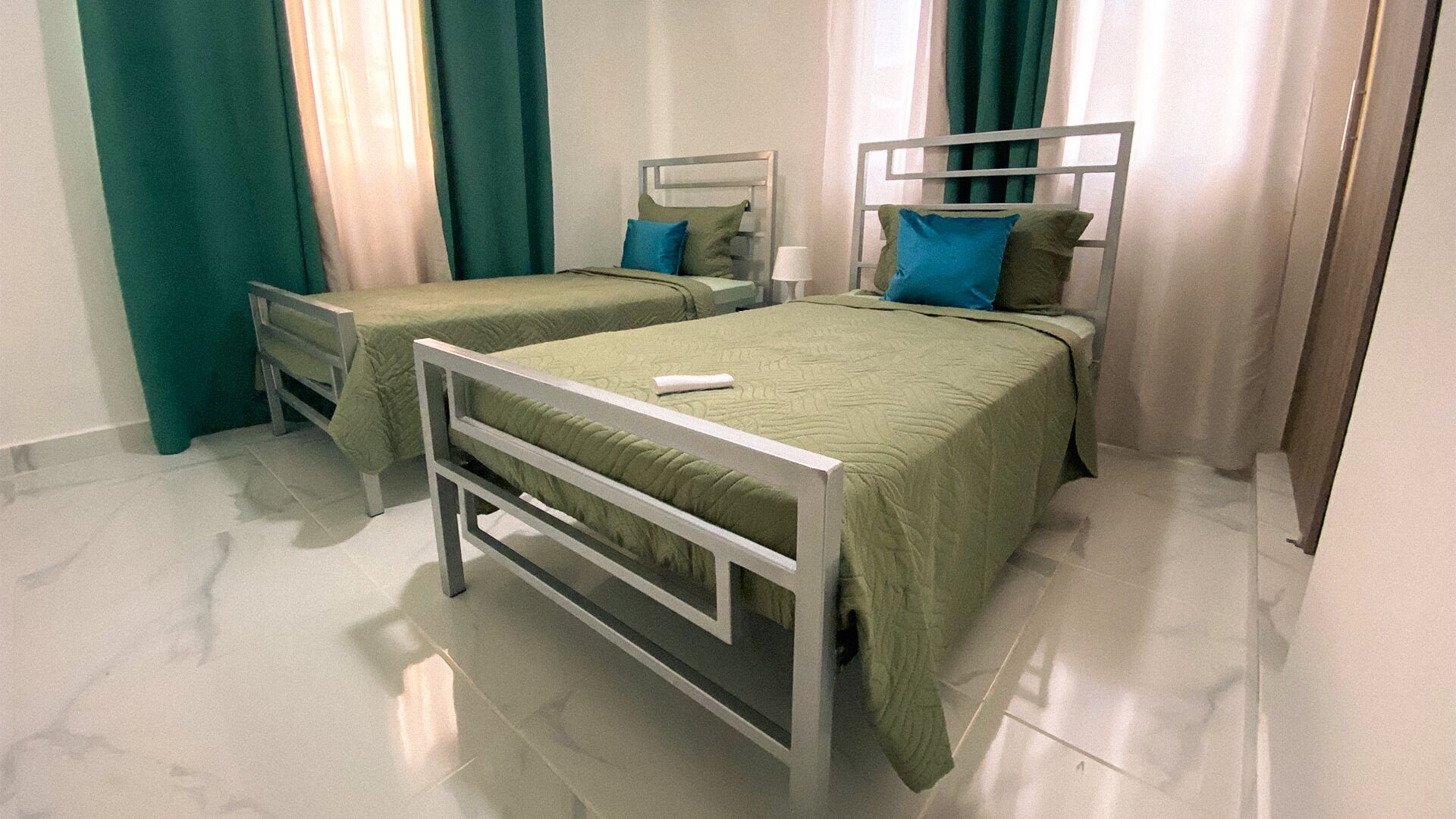 Une chambre d’hôtel avec deux lits simples, chacun doté d’un cadre en métal et de draps verts.