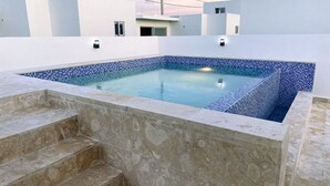 Ein rechteckiger Swimmingpool mit blauen Mosaikfliesen, umgeben von einer Steinmauer und Stufen zum Pool.