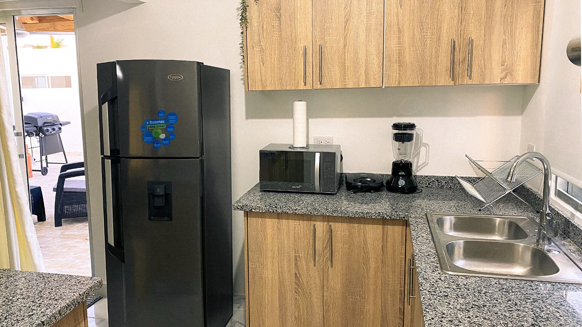 A compact kitchen with a stainless steel refrigerator, a microwave, a blender, and a sink.