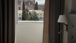 A hotel room with a bed, a window with curtains, a lamp, and a view of buildings and trees. - Camere con vista sul Chiostro Di Michelangelo (Rome)