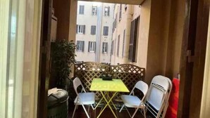 A small balcony with a yellow table and four chairs, a potted plant, and a view of a building with multiple windows. - Camere con vista sul Chiostro Di Michelangelo (Rome)