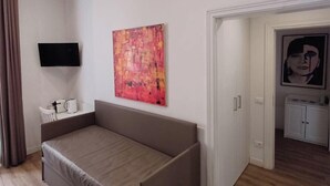 A modern hotel room with a bed, a flat-screen TV, an air conditioning unit, a painting, and a door leading to another room. - Camere con vista sul Chiostro Di Michelangelo (Rome)