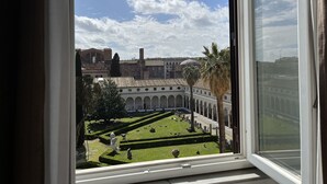 A view through a window of a courtyard with a building in the background, featuring a dome and arched structures. - Camere con vista sul Chiostro Di Michelangelo (Rome)