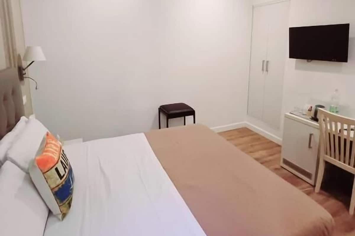 Una habitación de hotel con cama, escritorio, silla, televisor y armario.