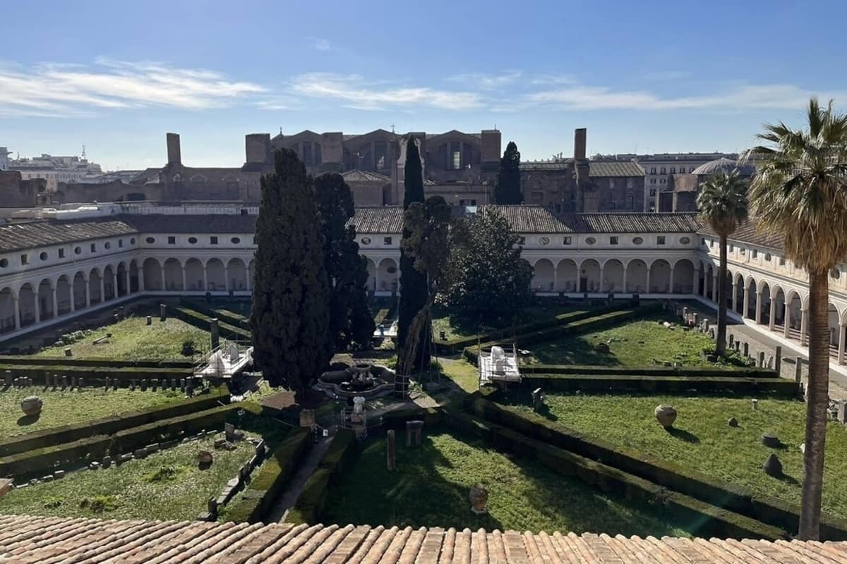 Un patio con una fuente, rodeado de edificios con paseos cubiertos y palmeras.