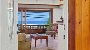 Una habitación con un amplio ventanal corredero que da a un balcón con vista al océano. Tiene techo de madera, un sofá y una mesa.