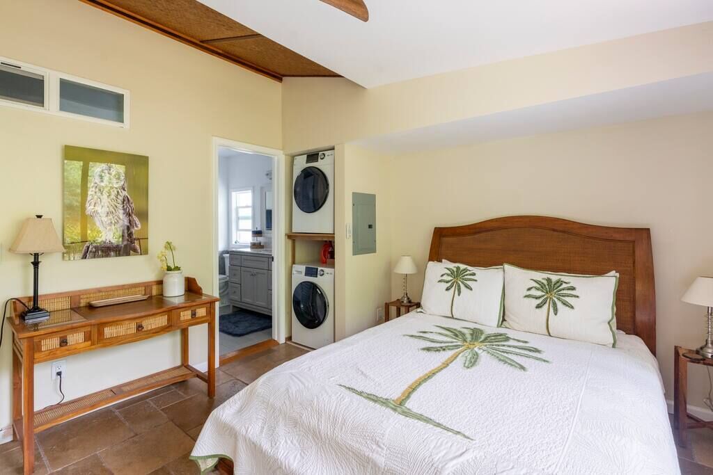 A bedroom with a bed, a wooden console table, a washing machine, and a painting on the wall.