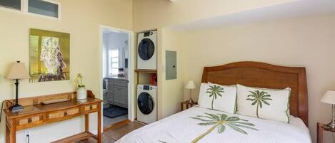 A bedroom with a bed, a wooden console table, a washing machine, and a painting on the wall.