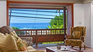 Una habitación con un ventanal grande que ofrece vistas al océano, techo de madera y un área de descanso con sofá y sillón.
