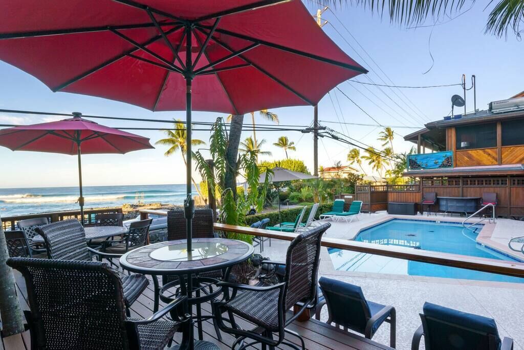 A poolside area with outdoor seating and umbrellas, overlooking a pool and ocean view.