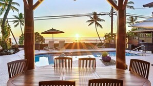 A wooden deck with a pool, lounge chairs, and a view of the sunset over the ocean. - Seahorse Luxury Suite at Seaspray Ocean View (Kahaluu-Keauhou)