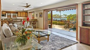 A spacious living area with a glass coffee table, a sofa, and a view of a pool and tropical landscape. - Seahorse Luxury Suite at Seaspray Ocean View (Kahaluu-Keauhou)