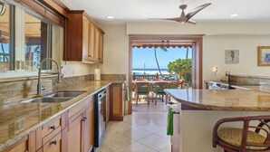 A kitchen with a large island, a dishwasher, and a view of the ocean through an open door. - Seahorse Luxury Suite at Seaspray Ocean View (Kahaluu-Keauhou)