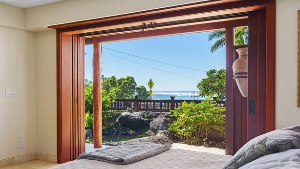 A bedroom with a large sliding glass door leading to a balcony with a view of the ocean and tropical vegetation. - Seahorse Luxury Suite at Seaspray Ocean View (Kahaluu-Keauhou)