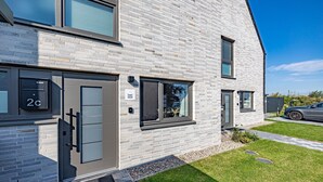 Un immeuble moderne à deux étages, avec une façade en briques grises, une boîte aux lettres bien visible portant le numéro 2C et une pelouse bien entretenue.