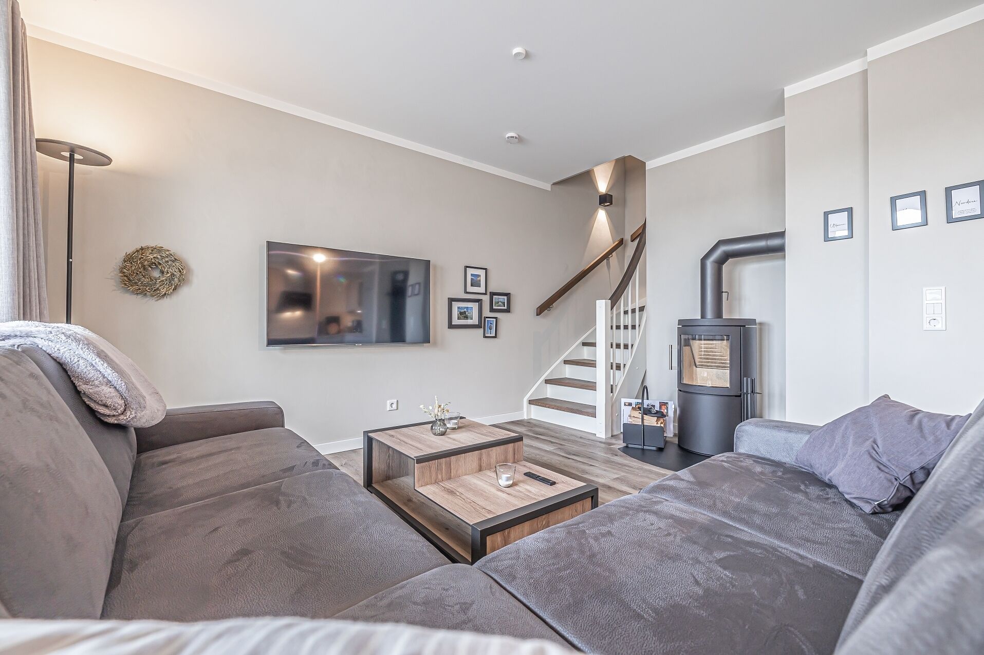 A modern living room with a grey sofa, a wooden coffee table, a flat-screen TV, and a staircase leading to a loft.