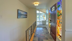 A hallway with a tiled floor, a wooden railing, a painting on the wall, and a stained glass door.